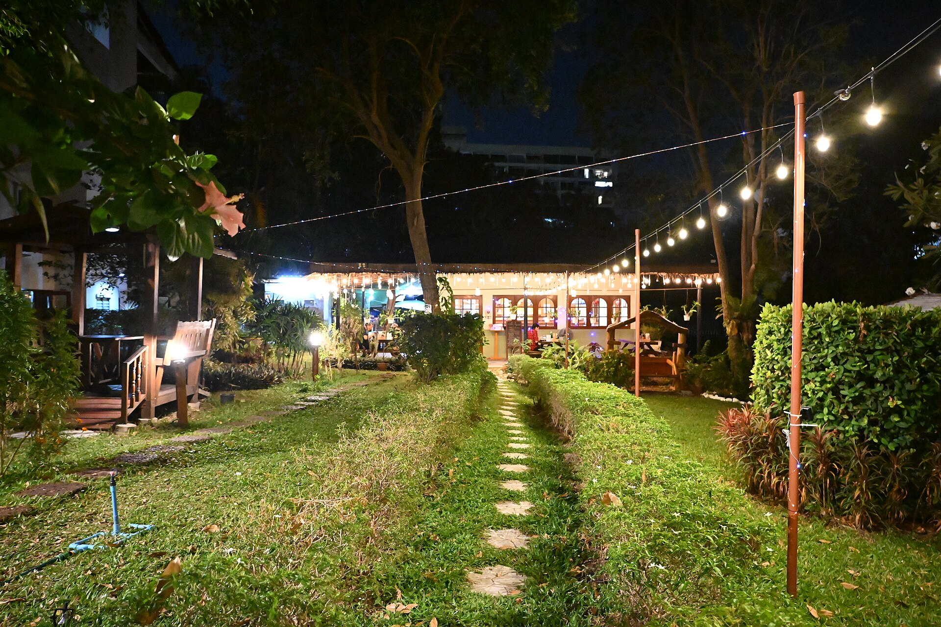 Allée de jardin en pas japonais éclairée le soir par des lampes sur piquets et des guirlandes