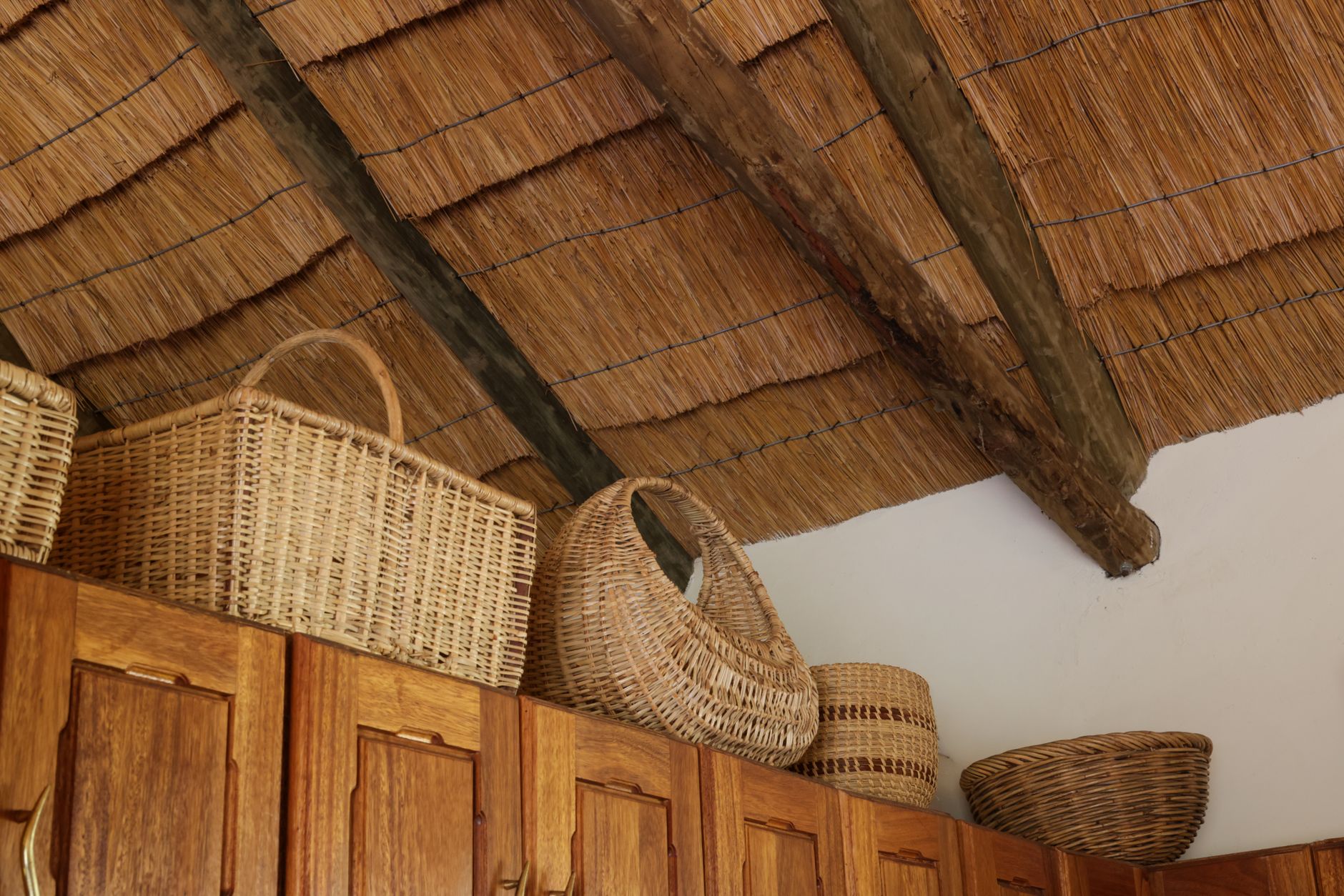 Paniers en osier posés au-dessus de placards de cuisine en bois sous un plafond en chaume.