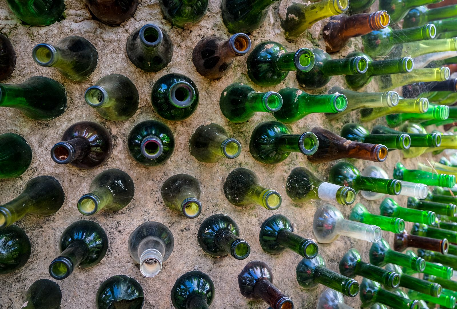 Un mur dont les bouteilles de verre vertes, brunes et transparentes sont enfoncées goulot vers l'intérieur, fonds tournés vers l'extérieur